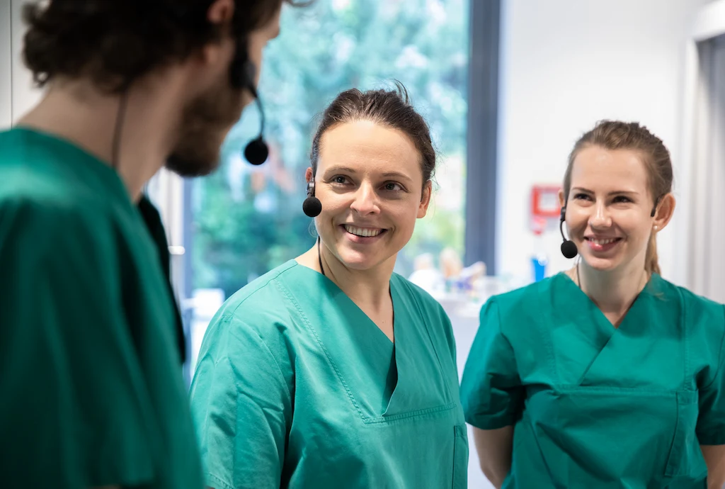Healthcare professionals in green scrubs with headsets discussing teamwork and communication in clinical training.