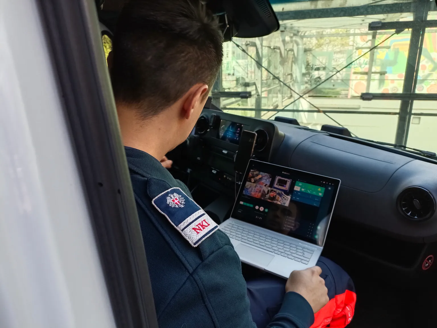 Emergency responder in uniform working on laptop inside service vehicle with monitoring dashboard interface.