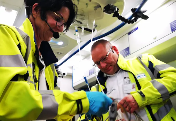 Emergency medical personnel in high-visibility jackets preparing equipment inside ambulance during simulation training.