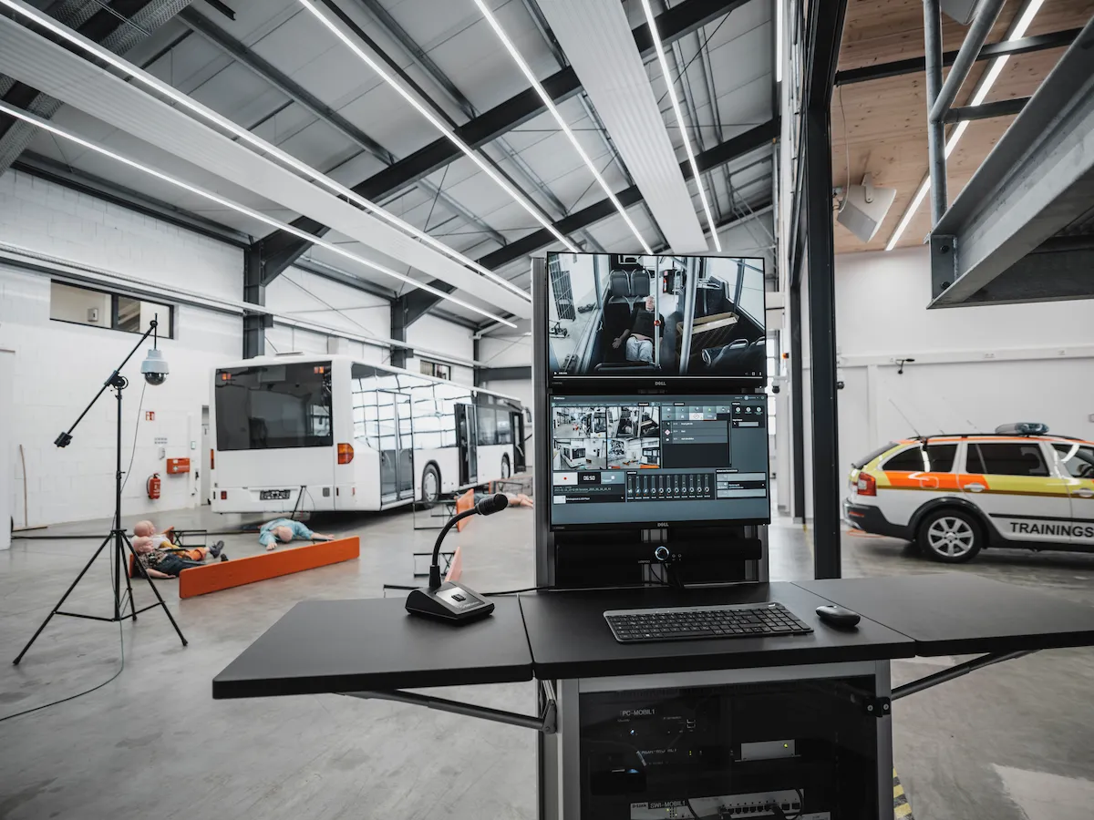 A contemporary debriefing room equipped with ergonomic tablet-arm chairs and a large wall-mounted interactive screen for reviewing recorded medical simulation data.