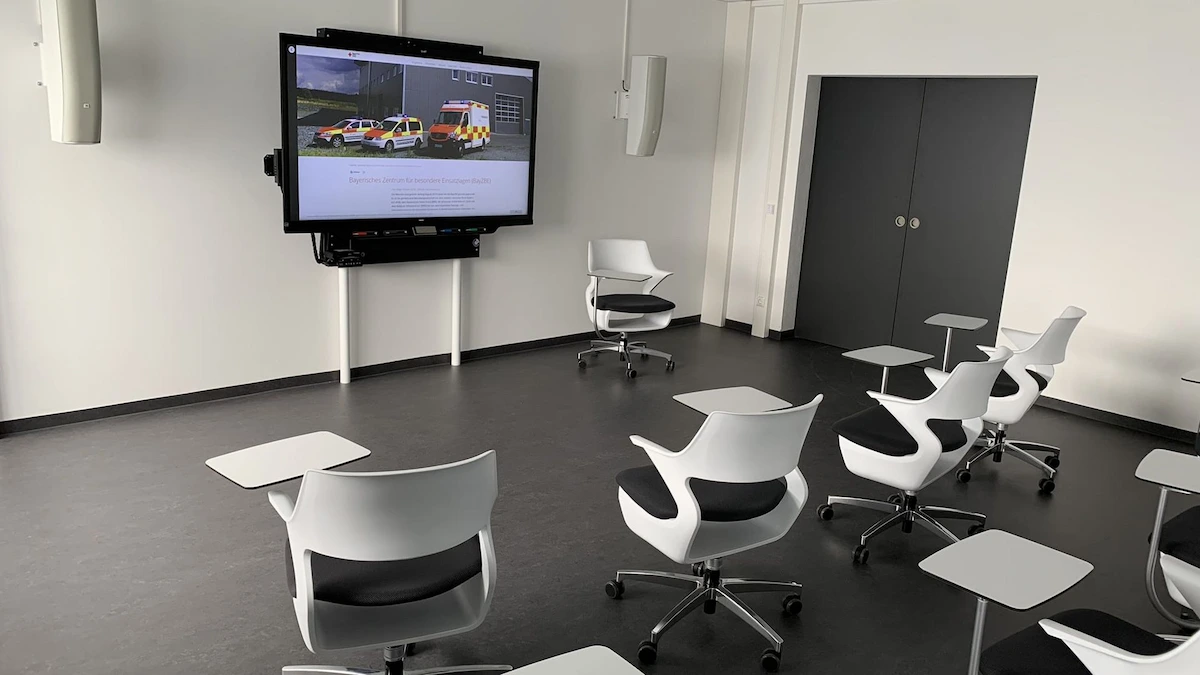 A sleek, modern debriefing room featuring ergonomic swivel chairs with tablet arms and a large wall-mounted interactive display for reviewing recorded simulation sessions.