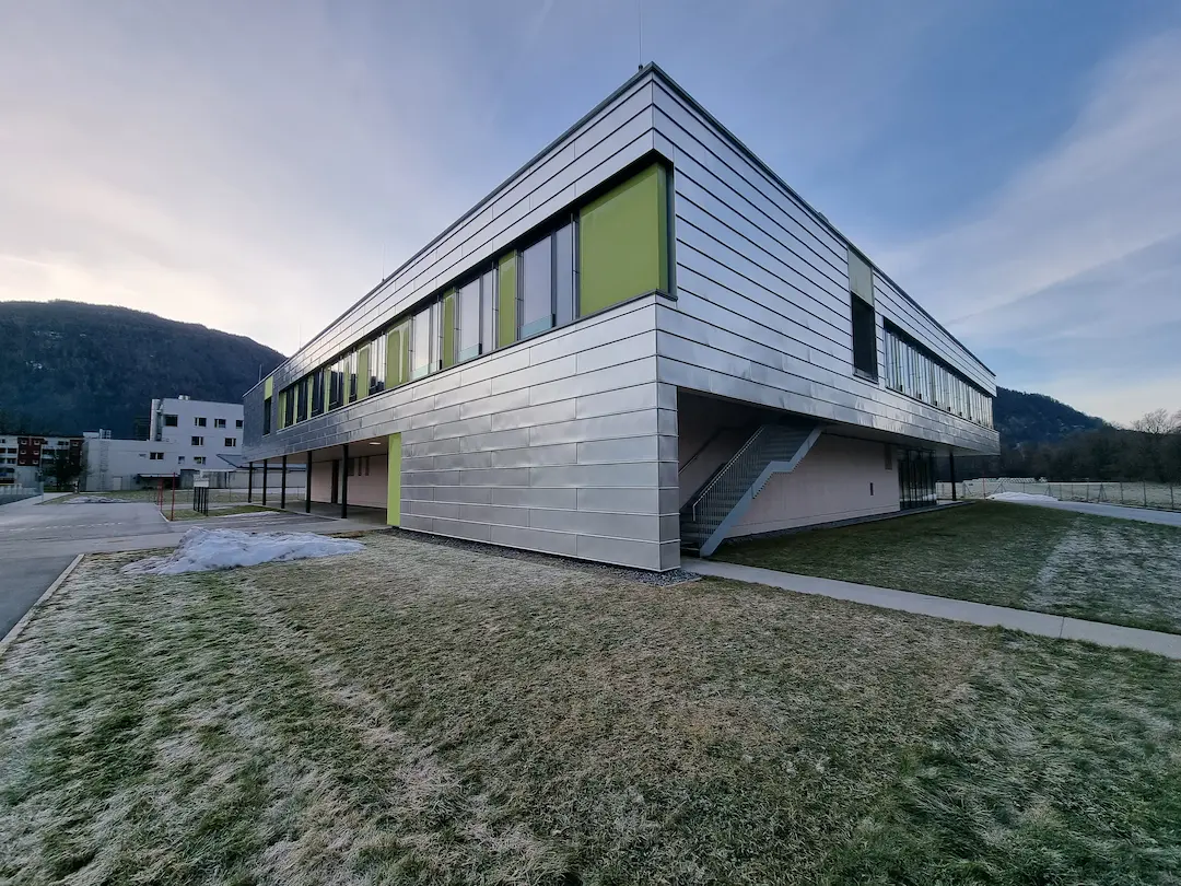 External view of a modern, metallic-clad medical simulation facility building featuring large windows and green accents, representing the state-of-the-art training environment.