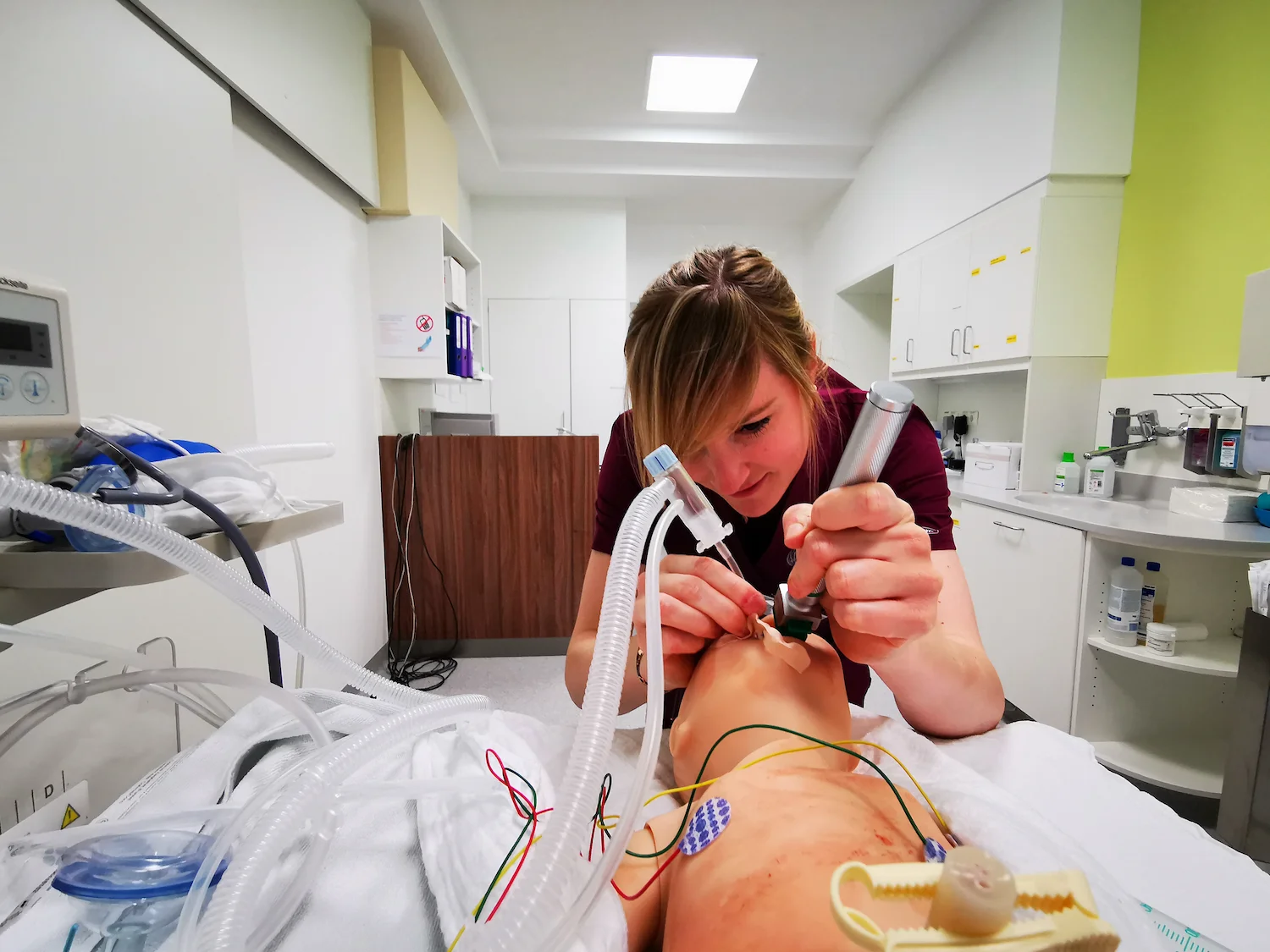 Close-up of a medical professional performing an endotracheal intubation on a high-fidelity patient manikin during a clinical simulation, featuring realistic medical tubing and monitoring sensors.