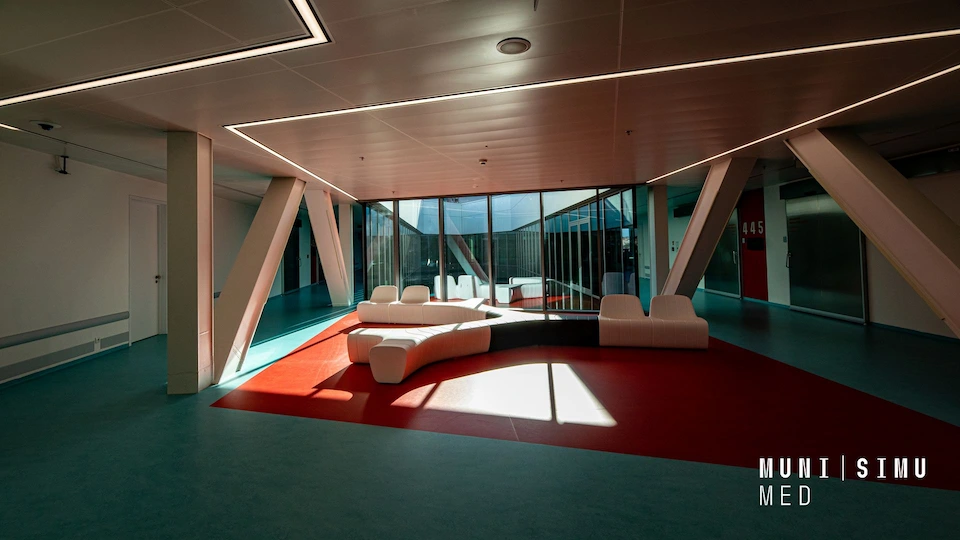 SIMU Brno Simulation Centre interior: modern lounge with white modular seating on a red carpet and glass walls.
