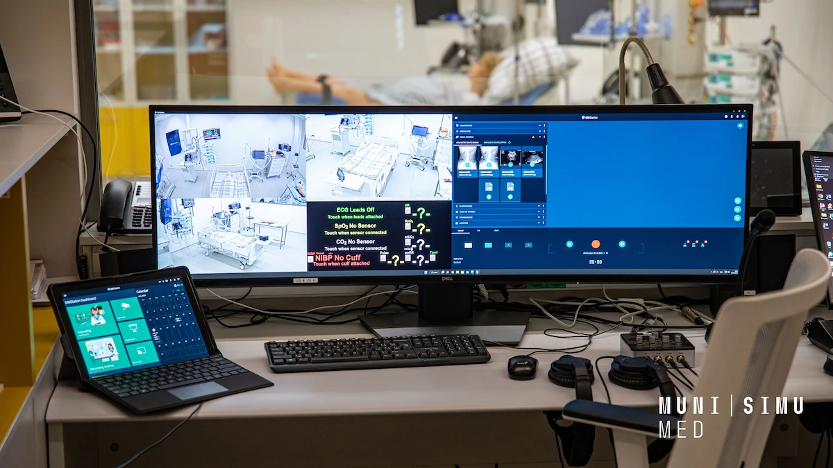 An ultra-wide monitor at the MUNI SIMU MED control center displaying a SIMStation interface with multiple live camera angles and real-time patient vitals from a medical simulation ward.