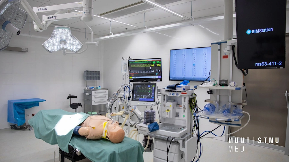 A high-tech medical simulation room at MUNI SIMU MED featuring a patient manikin on an operating table, integrated SIMStation recording monitors, and professional GE Healthcare anesthesia systems for clinical training.