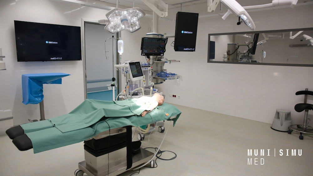 A wide-angle view of a high-tech operating theatre simulation room at MUNI SIMU MED, featuring a patient manikin on a surgical table, integrated SIMStation monitors for recording, and professional overhead surgical lighting.