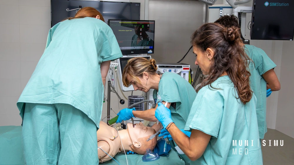 A medical team in teal scrubs at MUNI SIMU MED performing an intubation on a high-fidelity patient manikin, utilizing SIMStation recording technology for clinical skills assessment and team training.