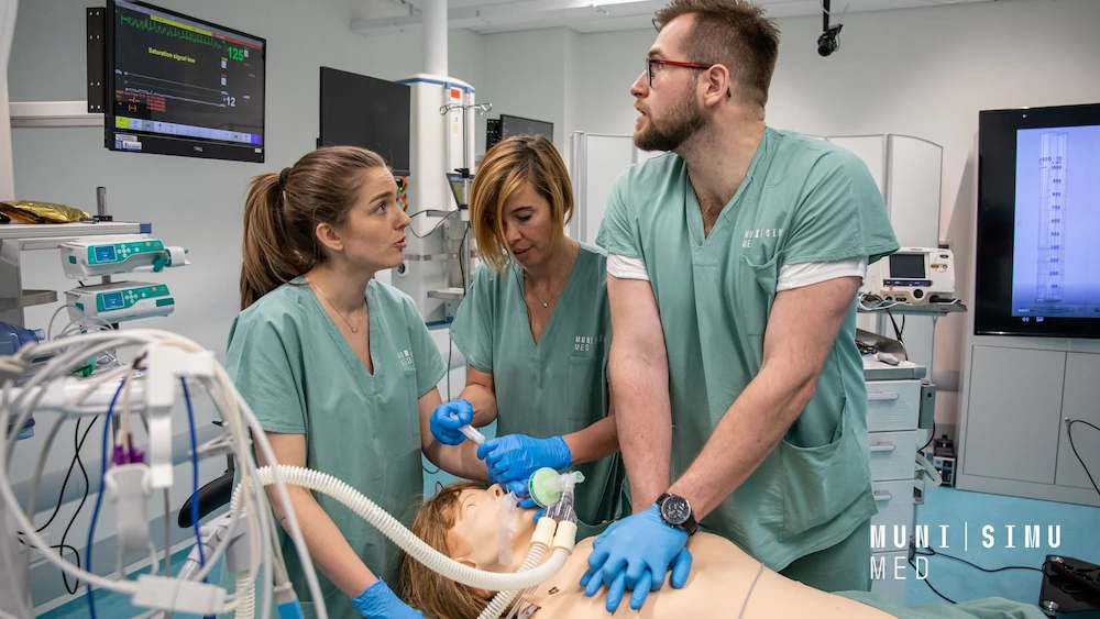 A medical team in teal scrubs at MUNI SIMU MED performing coordinated CPR and emergency airway management on a high-fidelity patient manikin, with real-time vitals monitoring displayed on an overhead screen.